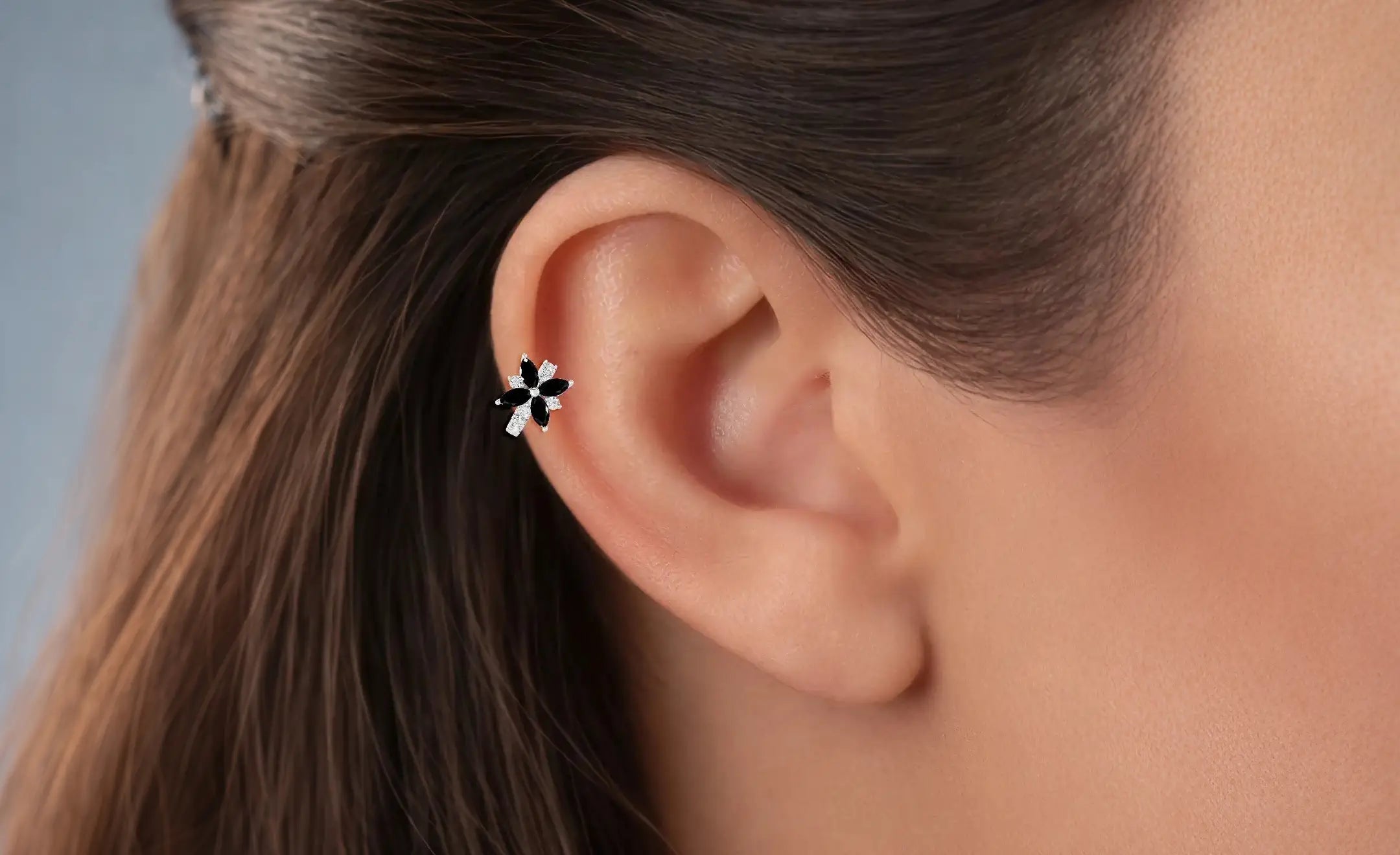 A close-up of a model's ear wearing a flower hoop black diamond earrings with diamond accents worn on the helix piercing