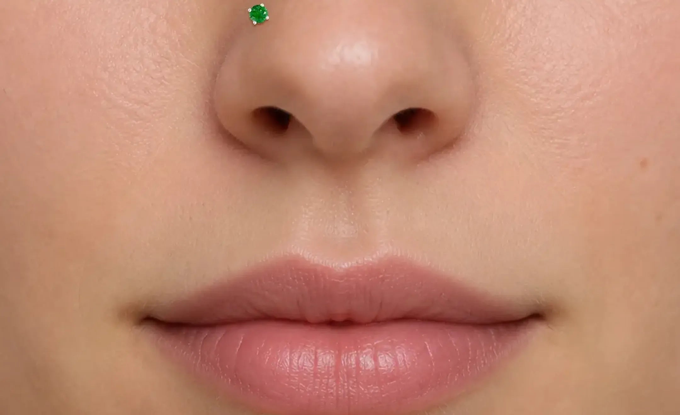 Extreme close-up of a person's lower face showing an emerald nose stud on the left nostril.