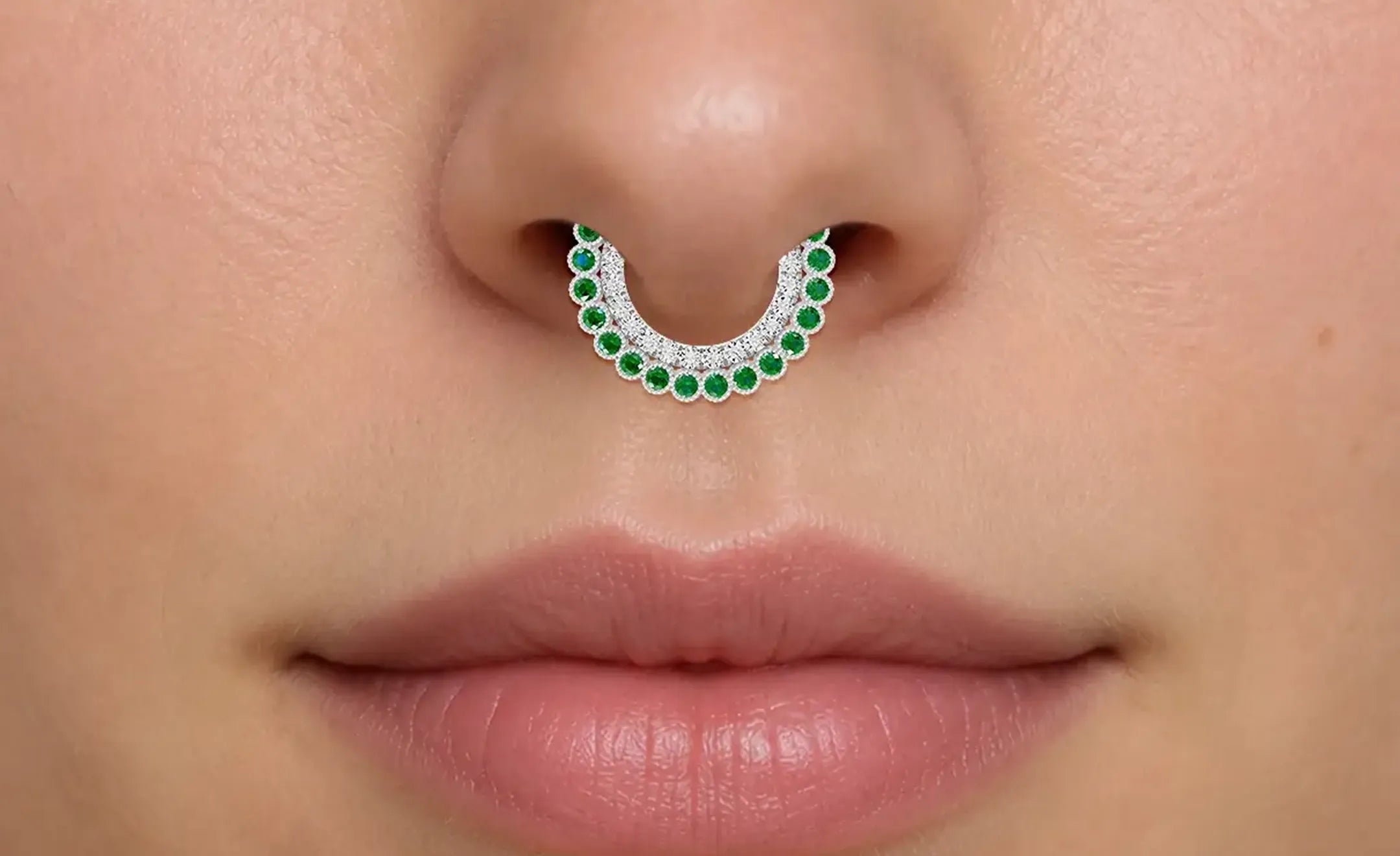 A close-up of a person's nose wearing an emerald with diamond accent nose ring worn on the septum piercing