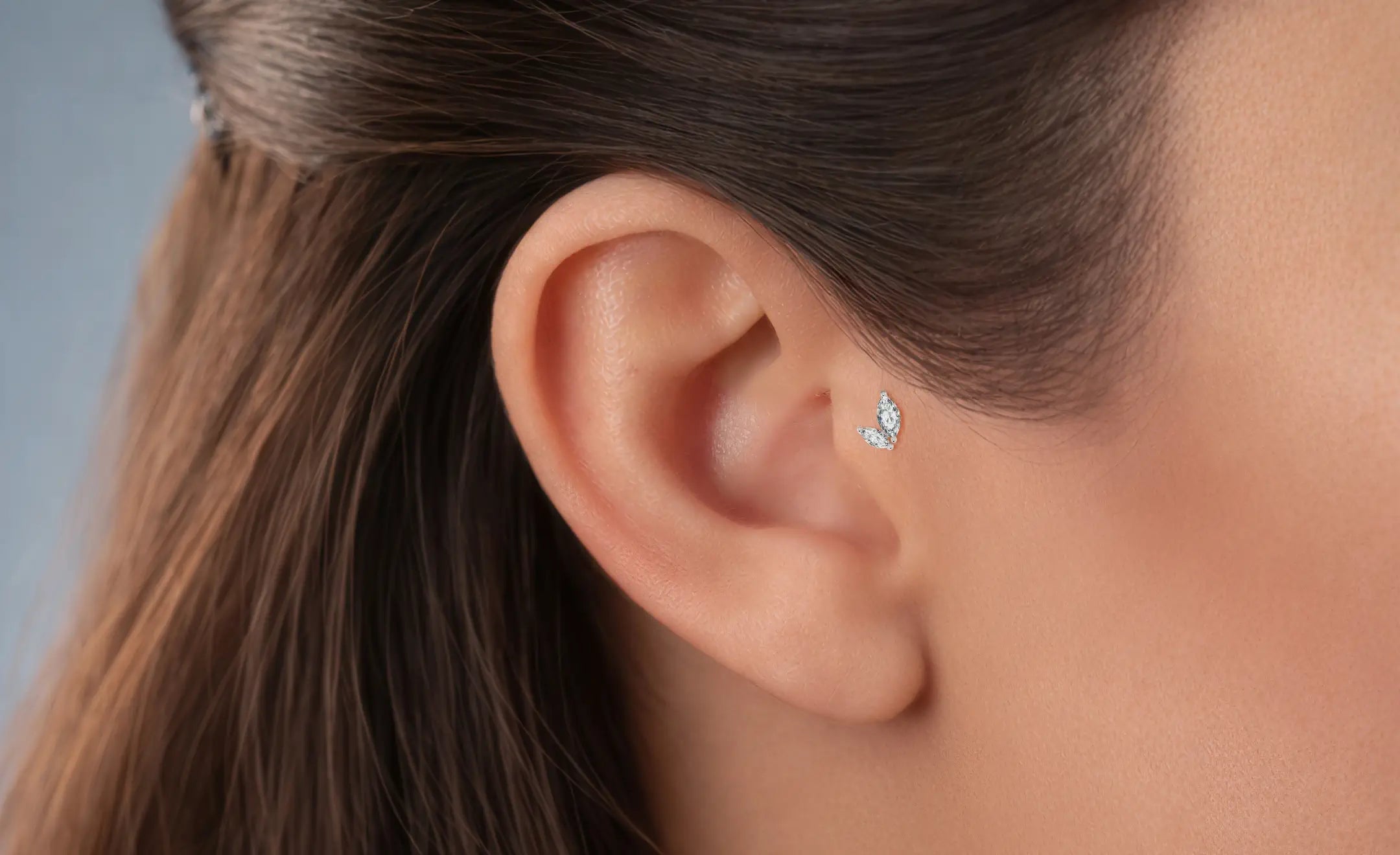 A woman's ear featuring a tragus diamond piercing against a grey background