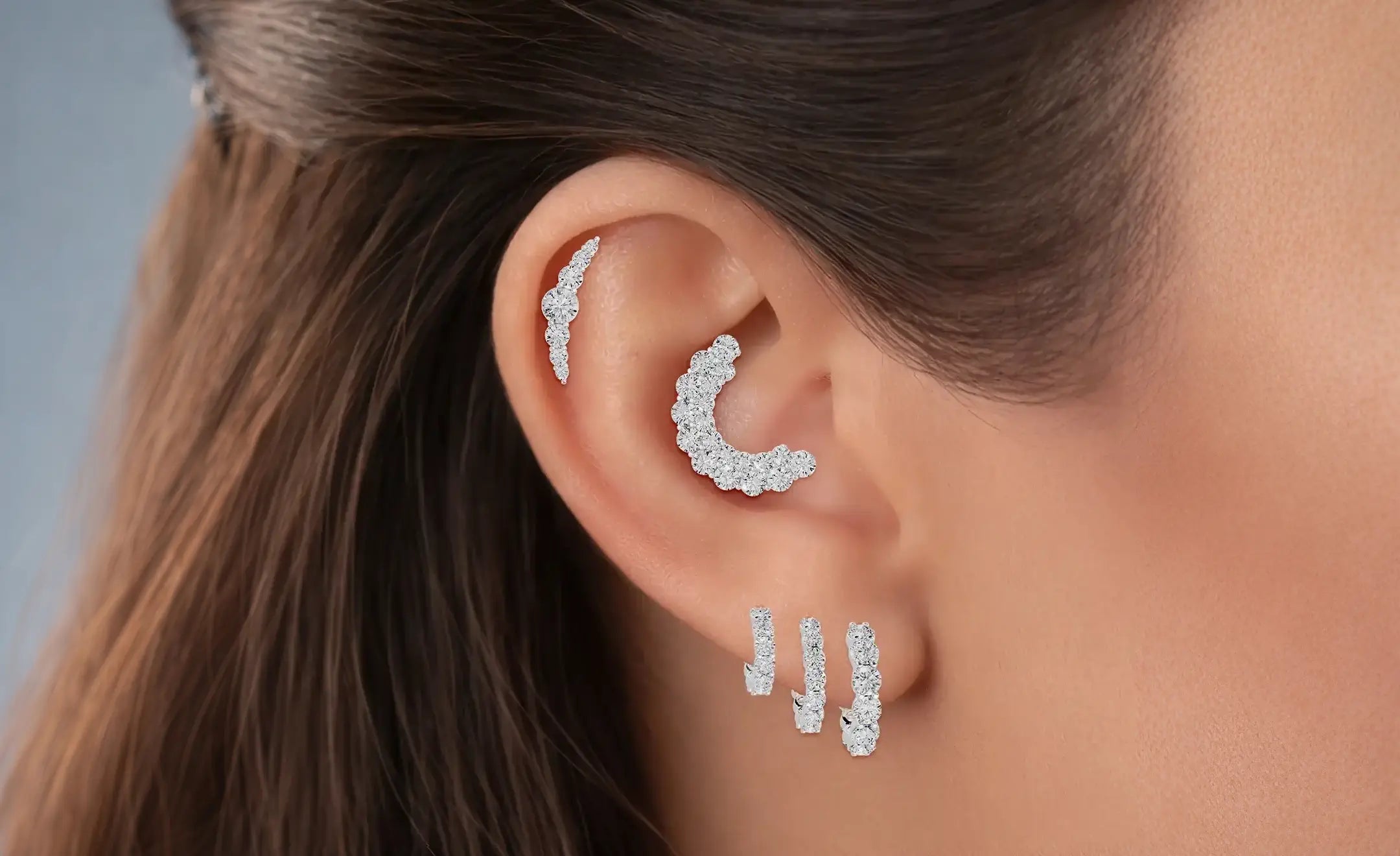 Ear stack of a women wearing diamond piercing. The white gold diamond hoop on the lobe in graduated size, a diamond ear climber, and last is a conch diamond piercing on the conch part. 