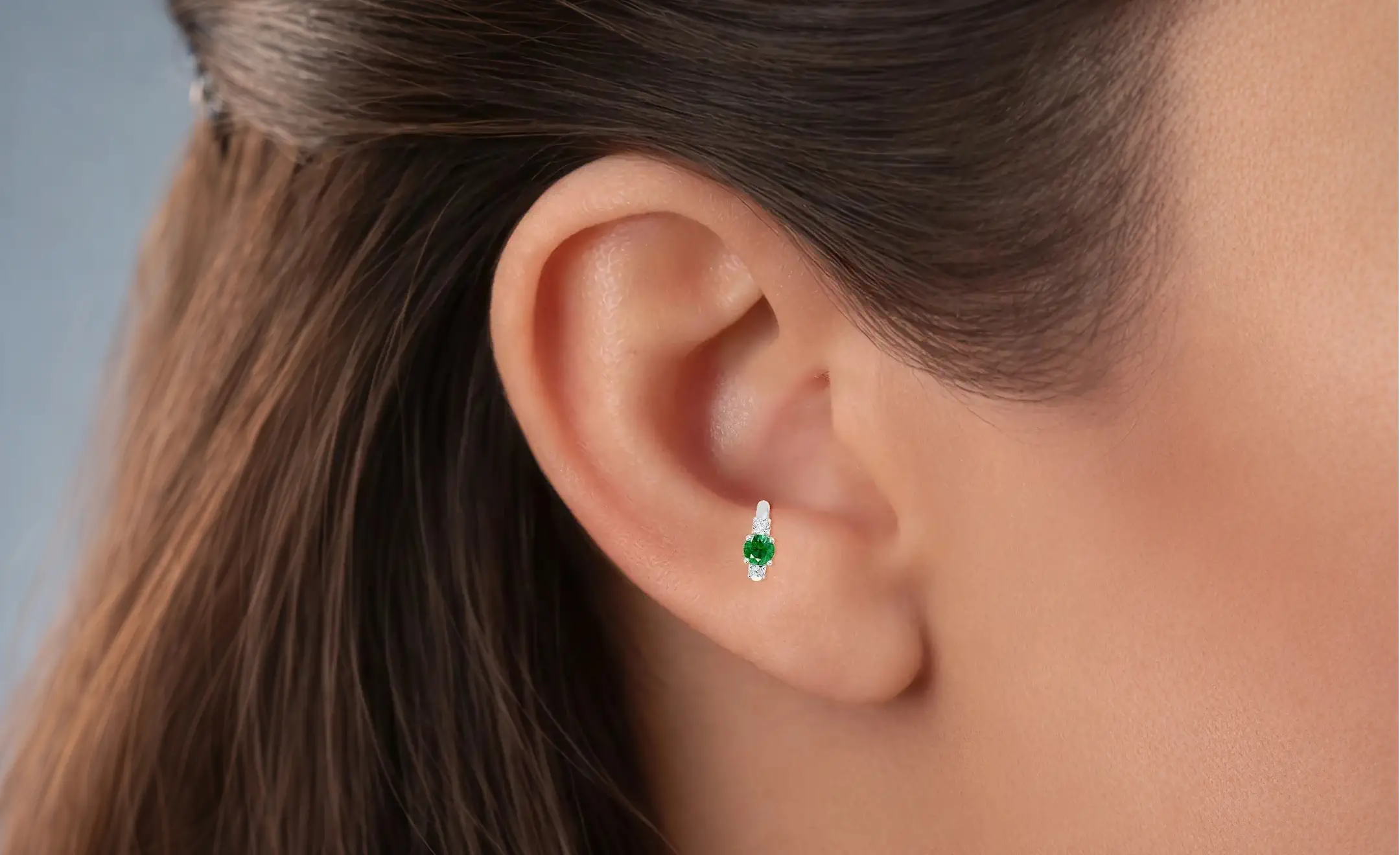A close-up of a person's ear wearing a small emerald hoop earrings in the antitragus piercing made in 18k gold
