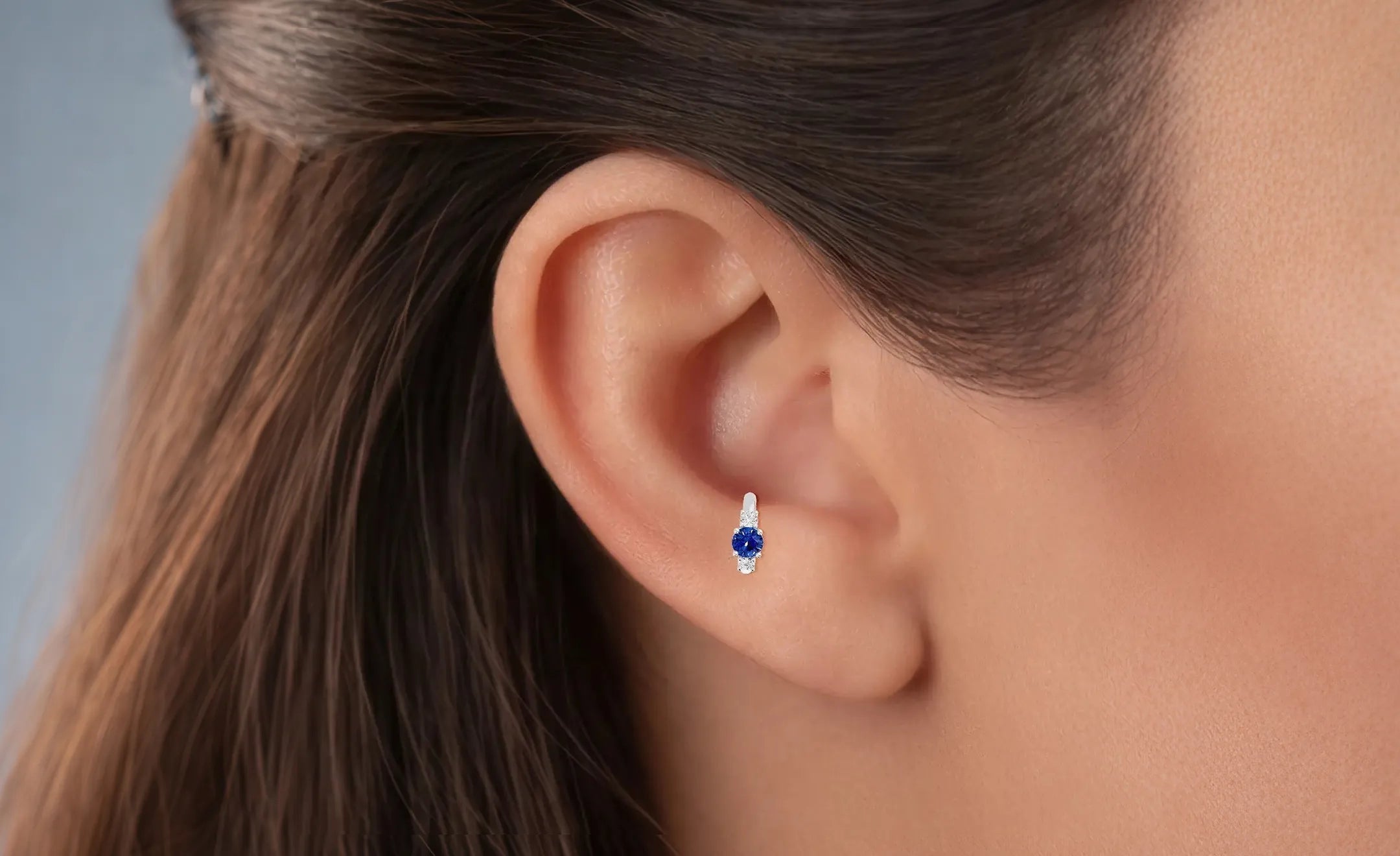 A close-up of a person's ear wearing a round sapphire hoop earrings with diamond accent worn on the antitragus piercing 