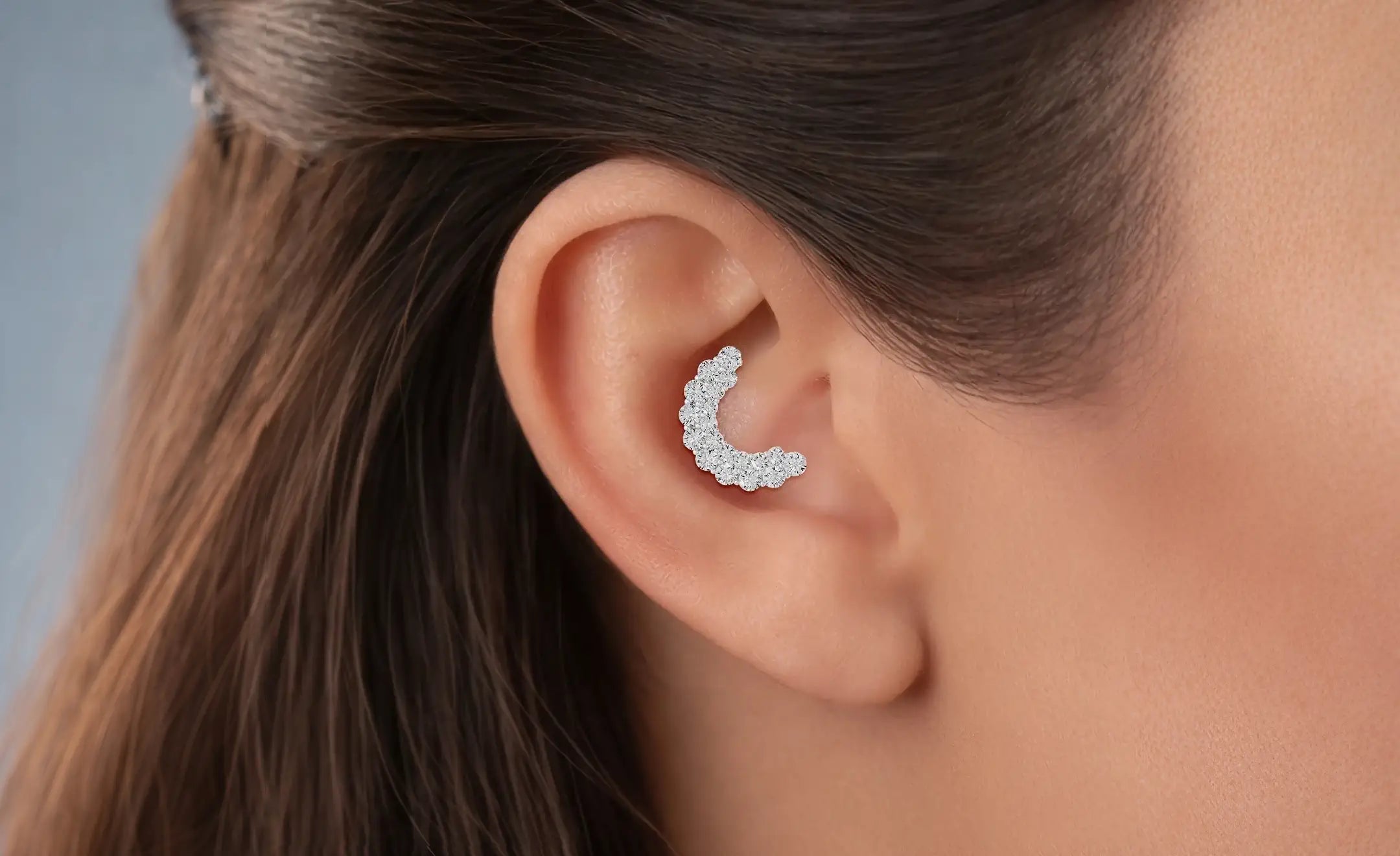A close-up of a woman's ear wearing a crescent-shaped stud earring set with diamonds made with 18k white gold worn on the conch piercing