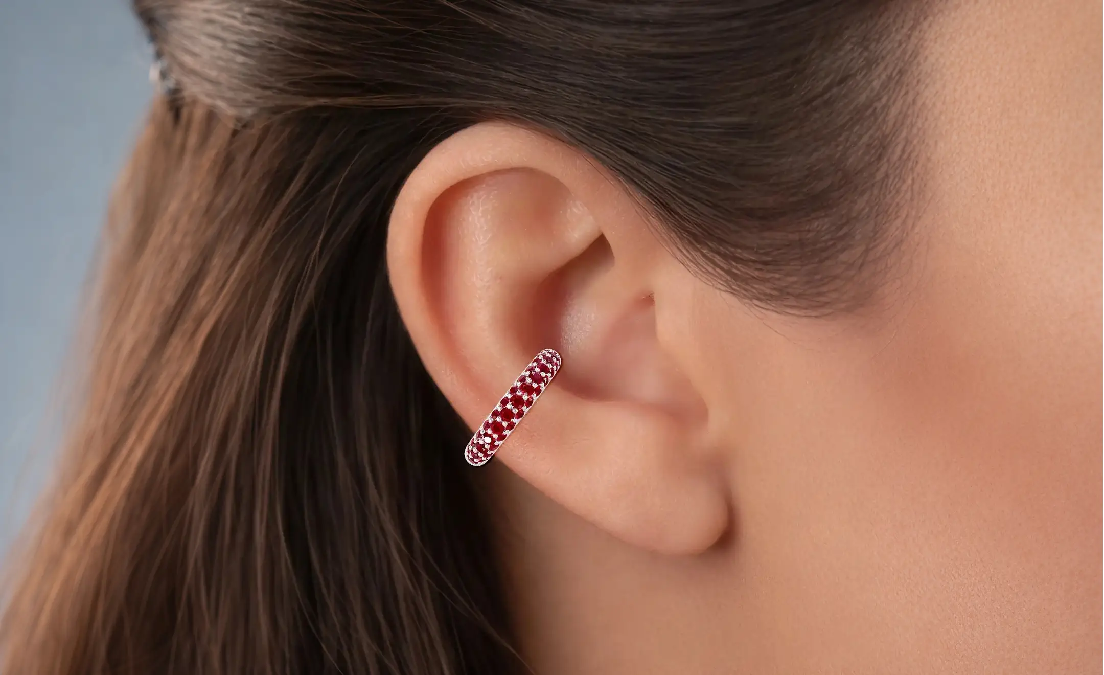 A close-up of a model's ear wearing a small ruby hoop earrings located at the conch piercing 