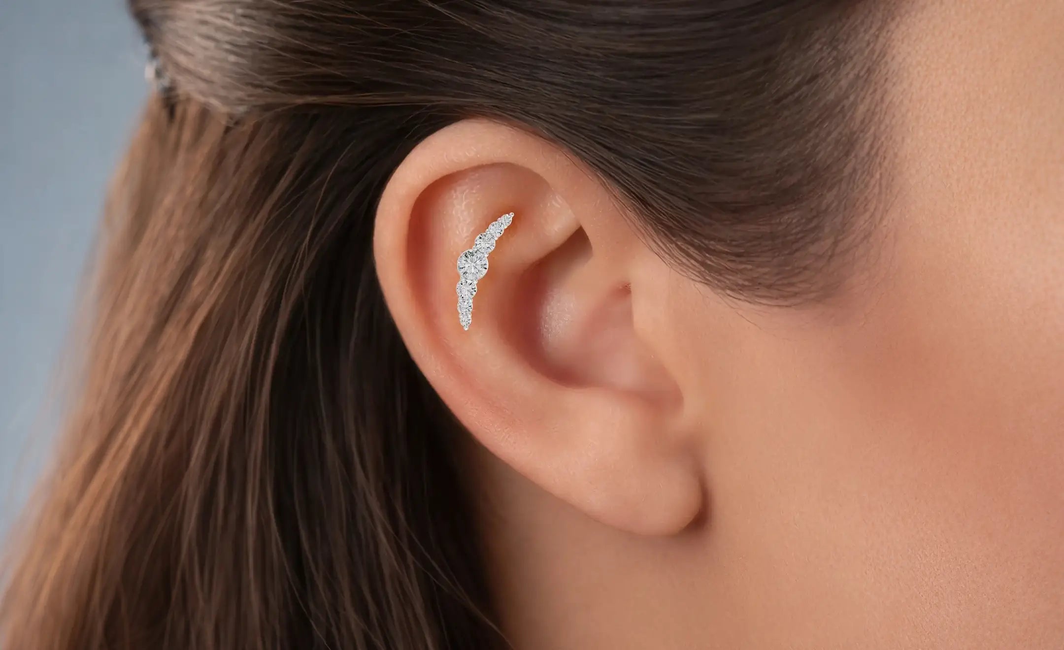 A close-up of a model's ear wearing a diamond ear climbers/walkers on the contraconch piercing 