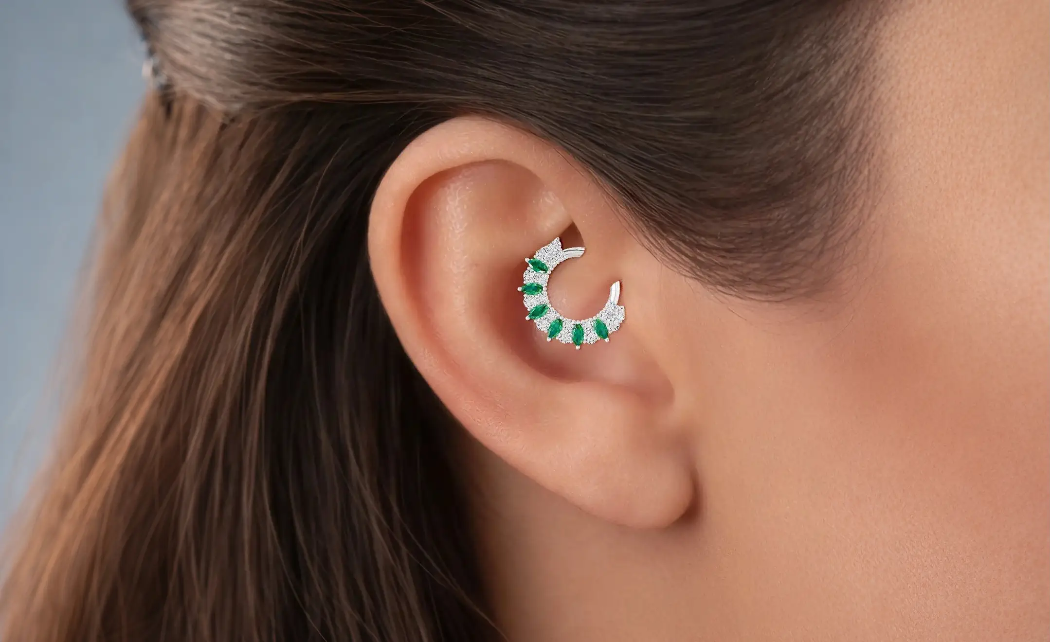 A close-up look on a person's ear wearing a combination of emerald and diamond daith rings on the daith piercing 