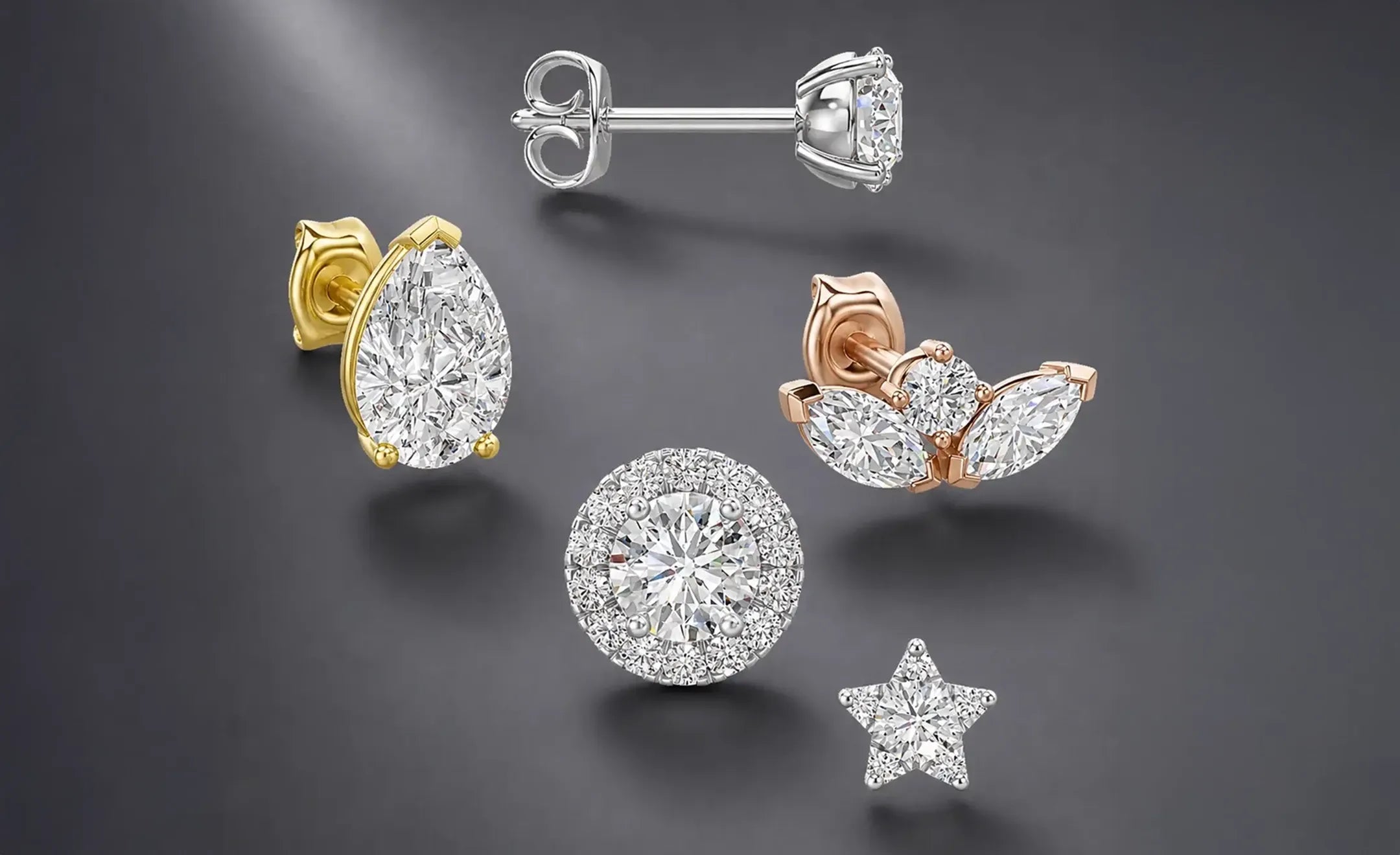A collection of five diamond stud earrings in yellow, rose, and white gold, displayed on a dark gray reflective surface. The designs include a pear, round halo, marquise lotus , and star shapes with butterfly back piercing