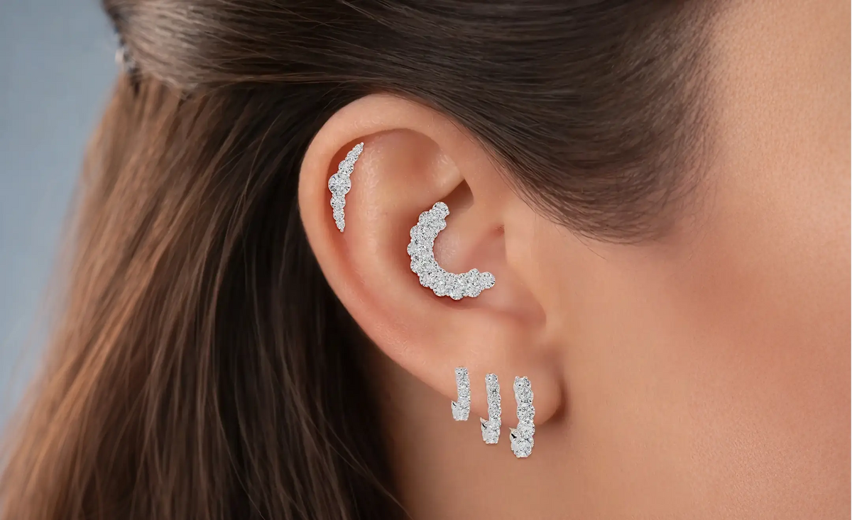 Close-up of a person's ear wearing multiple 18k white gold earrings in a form of studs and hoops with diamonds 