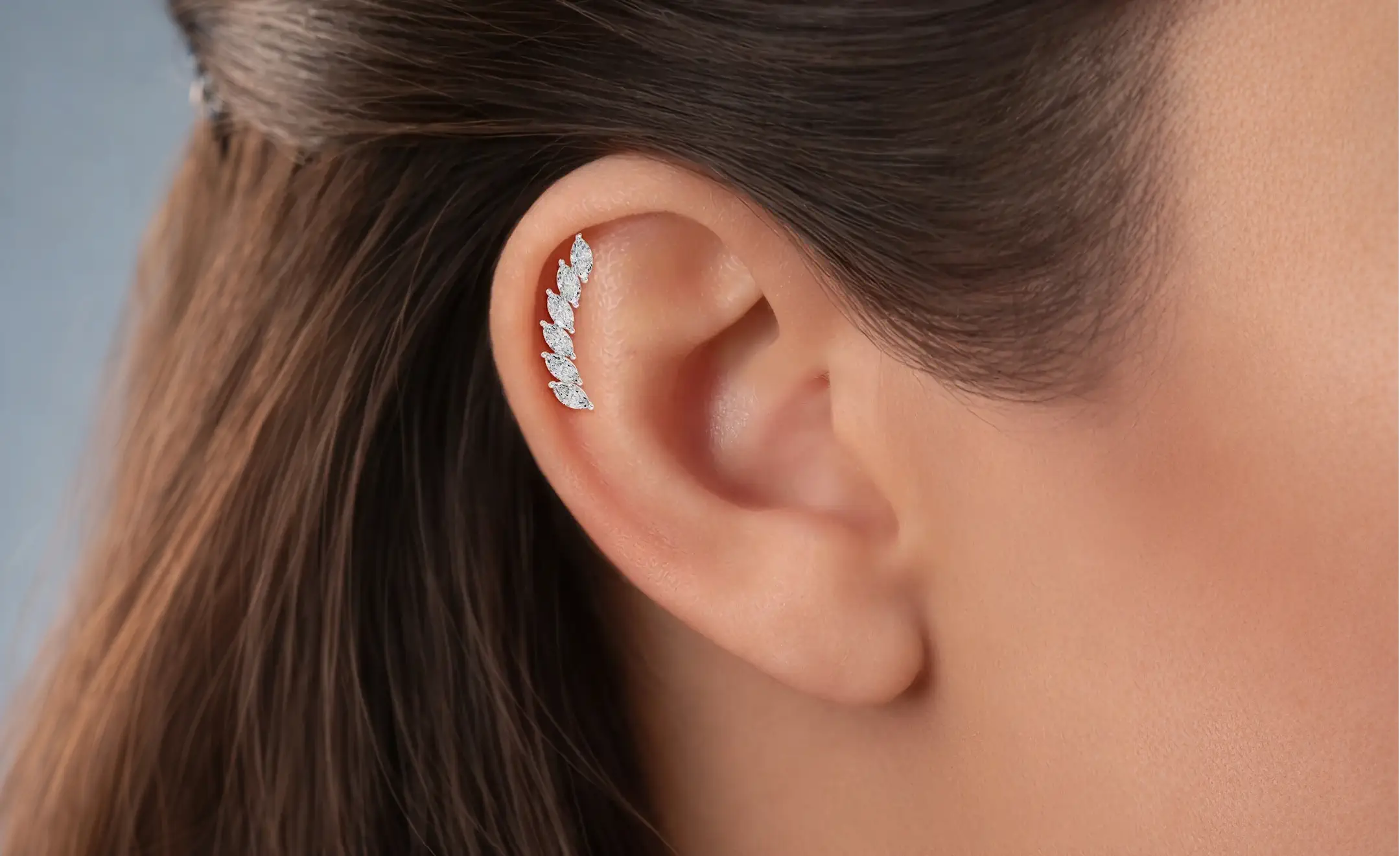 A close-up look of a girl's ear wearing a diamond marquise ear climber stud earring on the helix piercing