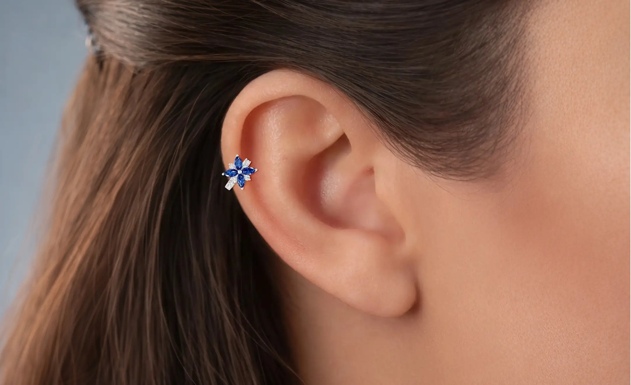 A close-up of a model's ear wearing a flower sapphire with diamond accent hoop earrings on the helix piercing