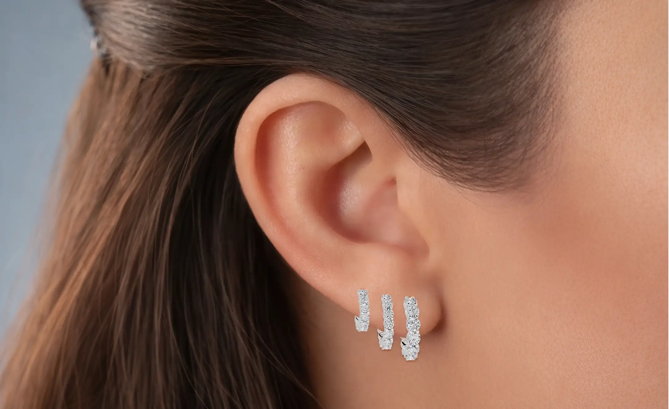 A close-up of a woman's ear wearing three diamond hoop earrings on the lobe in graduated size 
