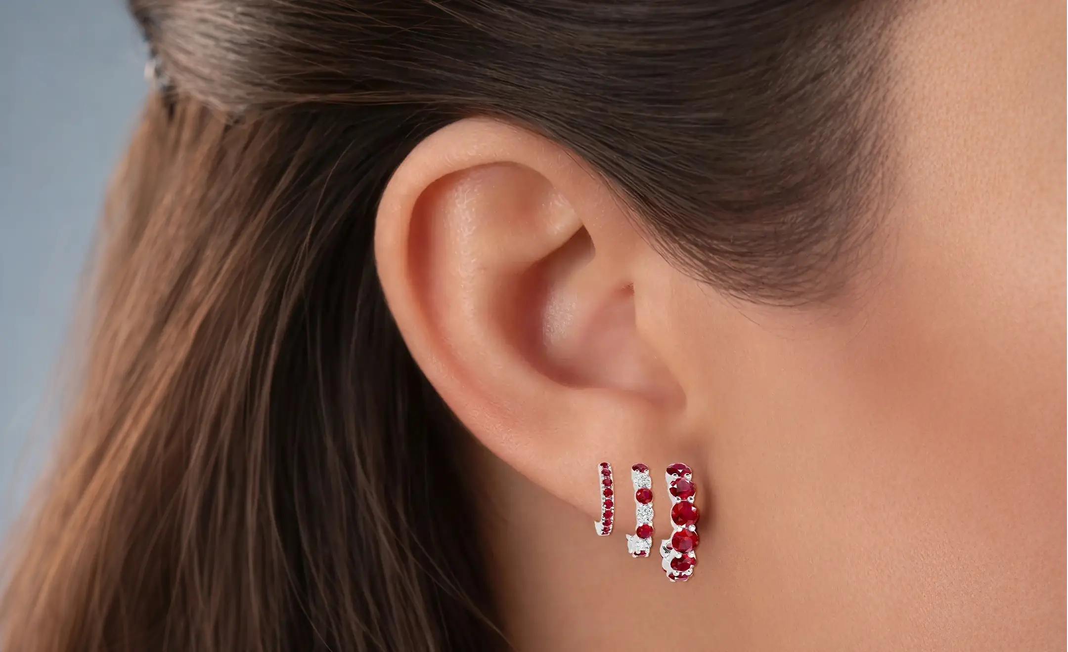 A close-up of a person's ear wearing an 18k white gold ruby hoop with diamond accent on the middle hoop worn on the lobe 