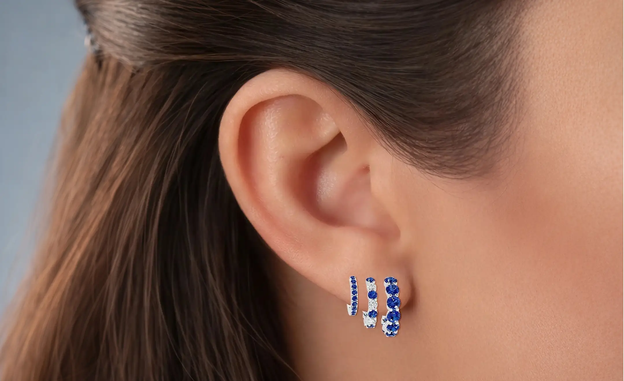 A close-up look of a woman's ear wearing a sapphire hoop earrings in graduated size worn on the lobe part