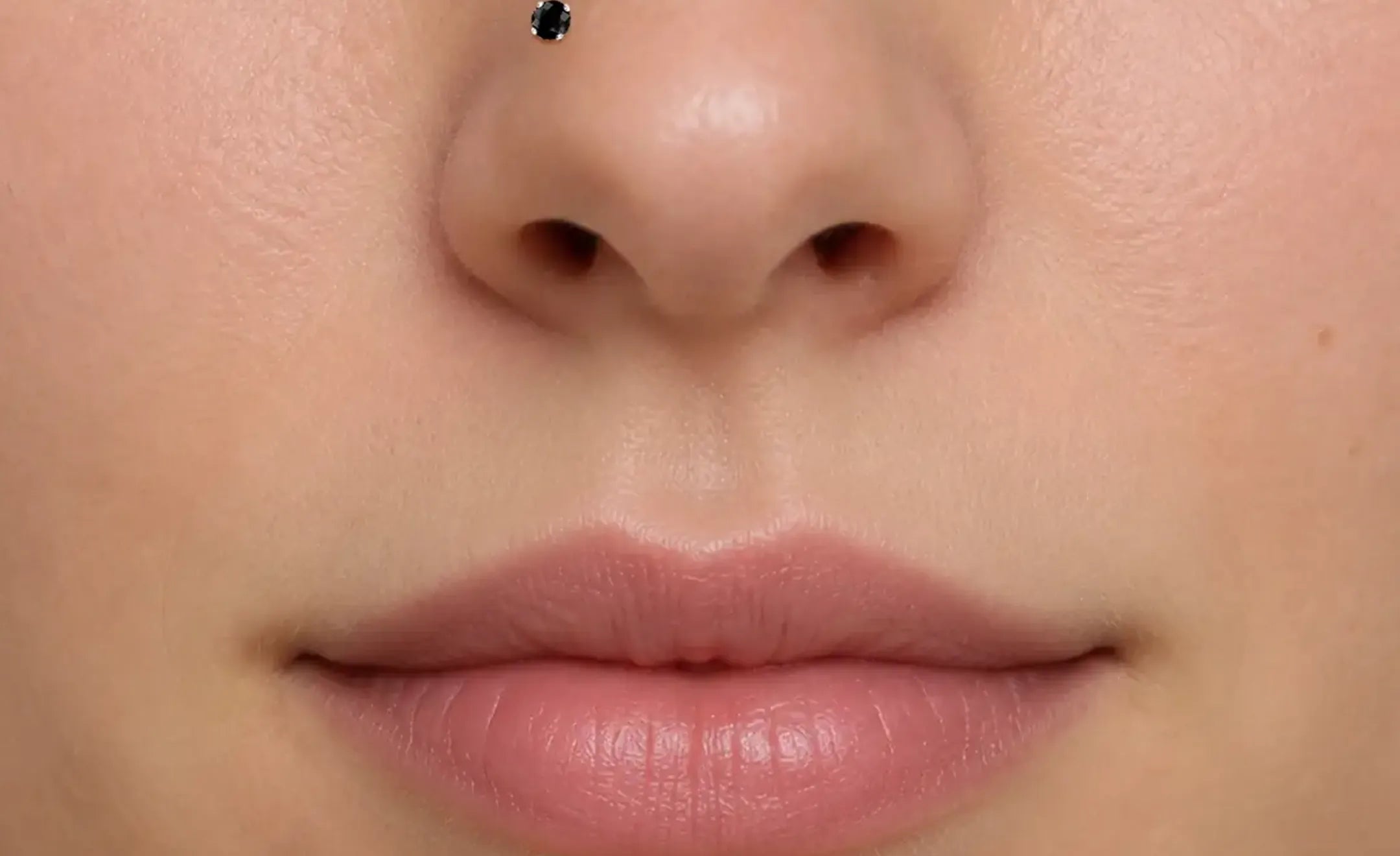 Extreme close-up of a person's lower face showing a small black diamond nose stud on the left nostril.
