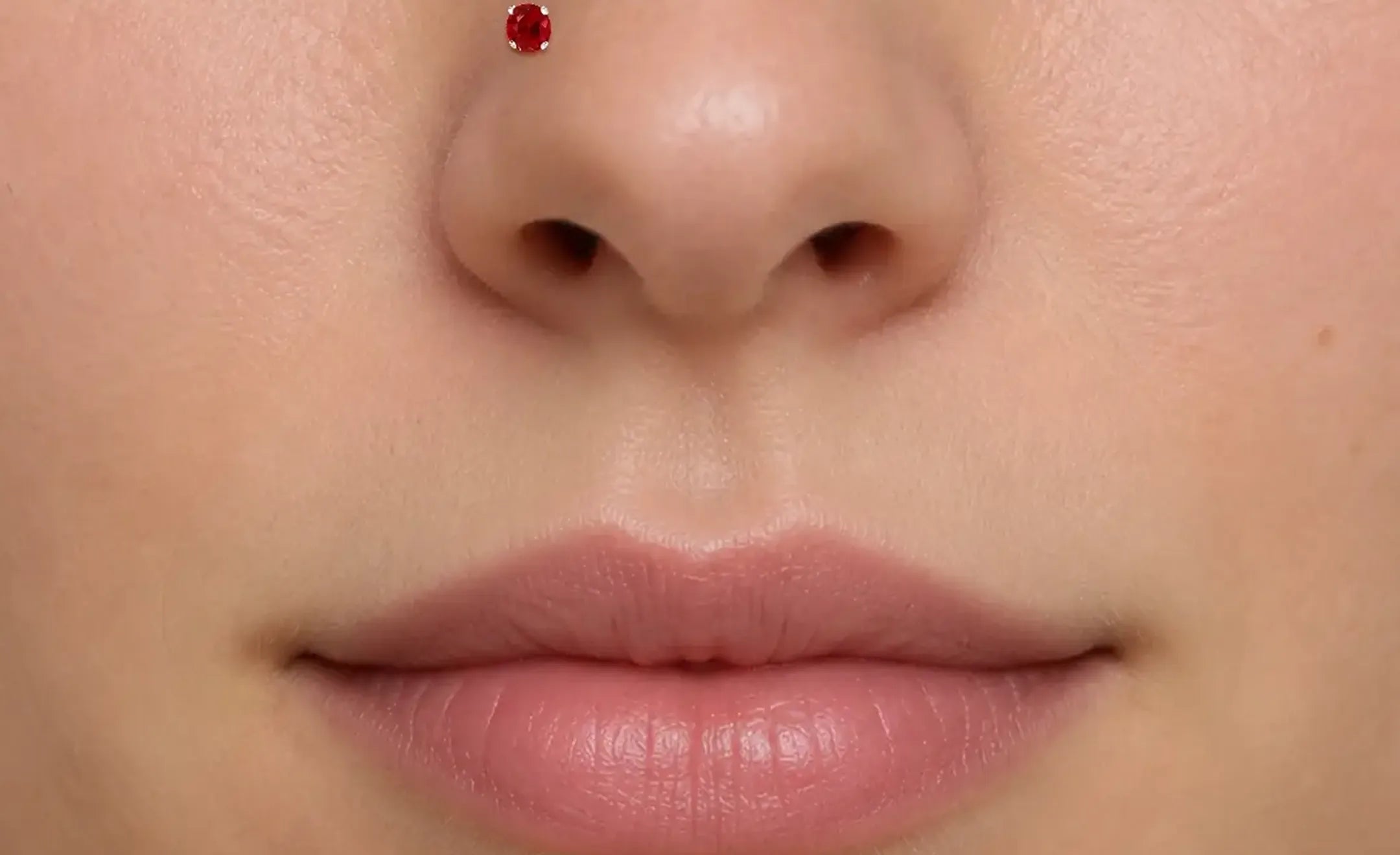 Extreme close-up of a person's lower face showing a ruby nose stud on the left nostril.