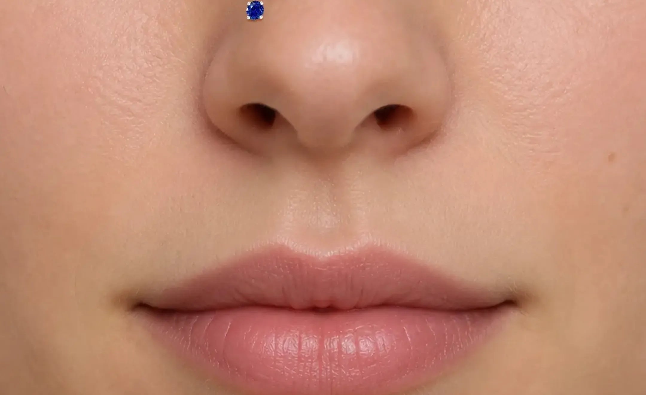 Extreme close-up of a person's lower face showing a blue sapphire nose stud on the left nostril.