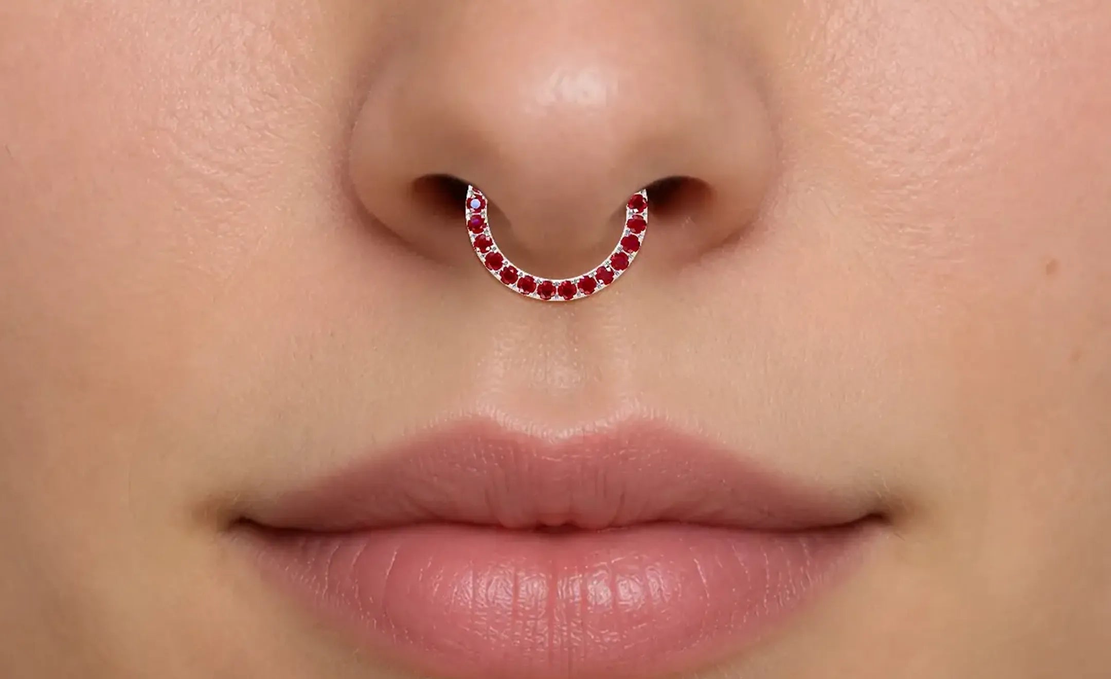 A close-up of a person's nose wearing ruby nose ring worn on the septum piercing 
