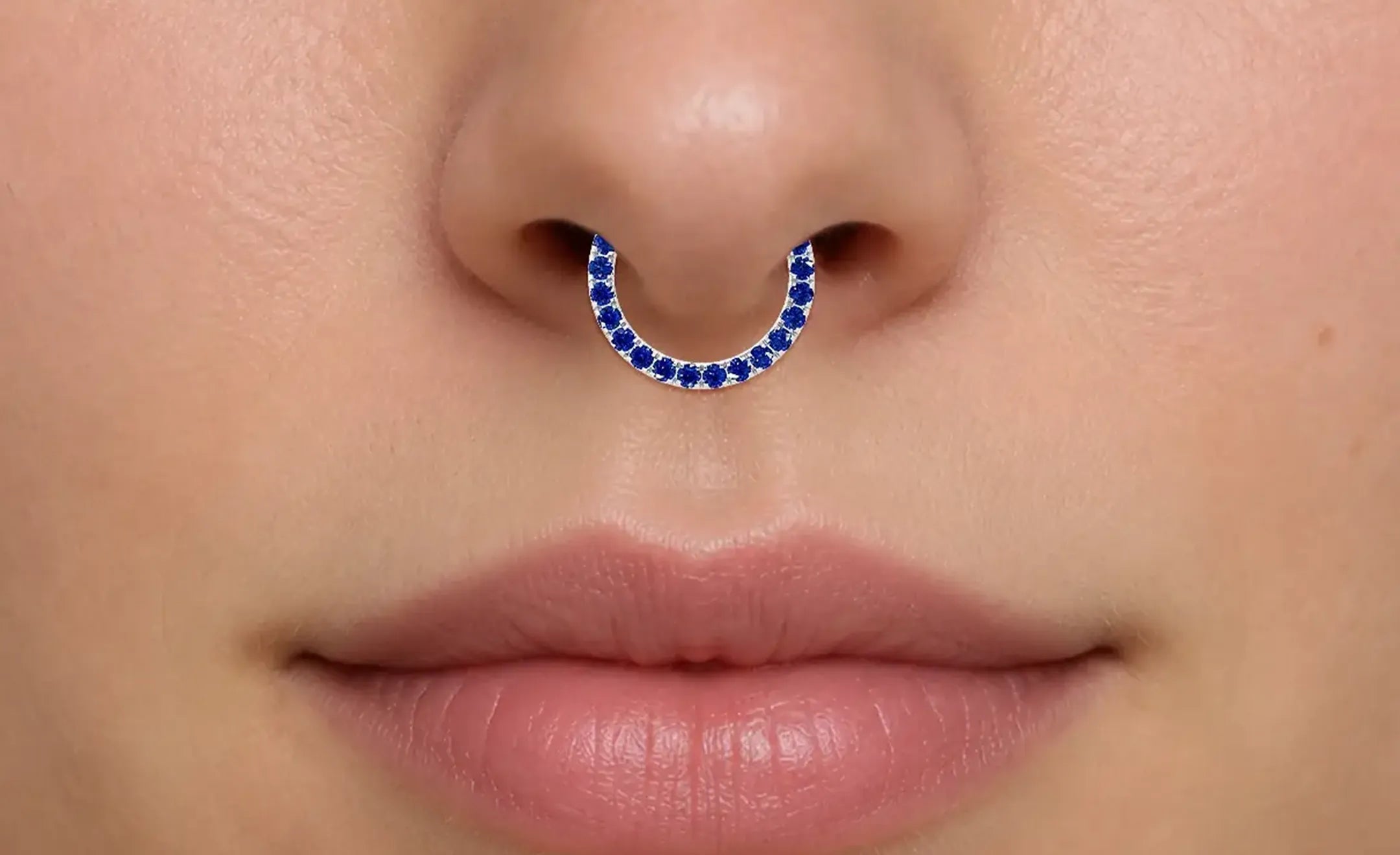 A close-up of a person's nose wearing a blue sapphire nose ring on the septum 